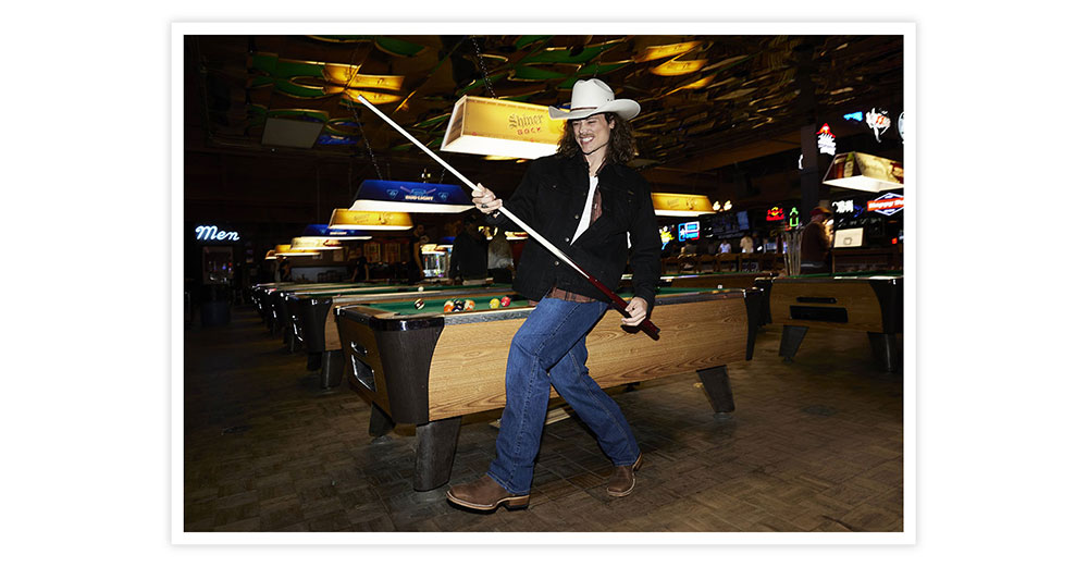 A man wearing Jackpot 11” Western in brown holding a pool stick, playing pool.